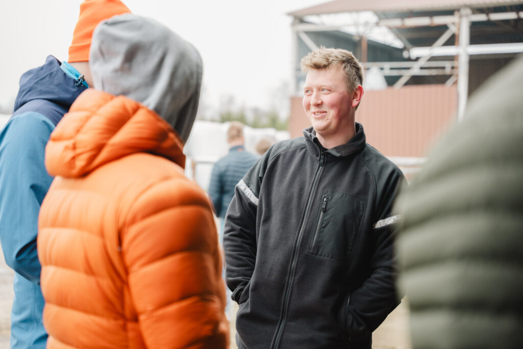 En glad BUer smiler til andre BUere på et gårdsbesøk. Vi ser kun ryggen til de andre.
