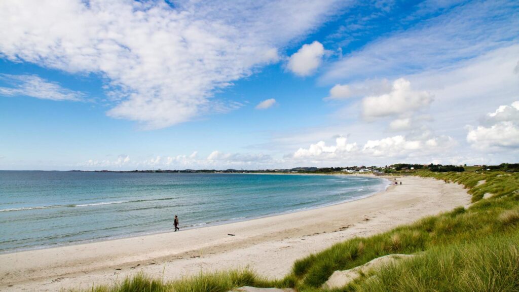 Bilde av en strand på Jæren. Det er sol med noen skyer. Stranden er en sandstrand.